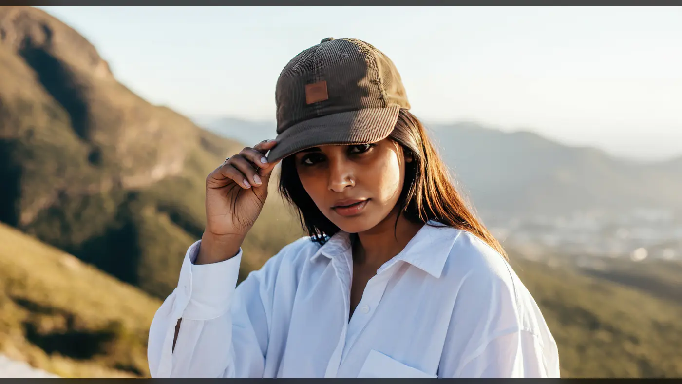Confident Woman in Cap and White Shirt with Mountain Backdrop
