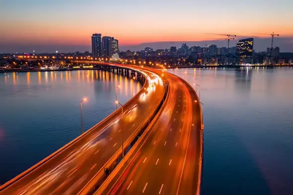 Curved Highway Bridge Over Water at Sunset with City Skyline