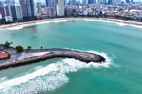 Aerial View of Urban Beach with Rocky Breakwater and Cityscape