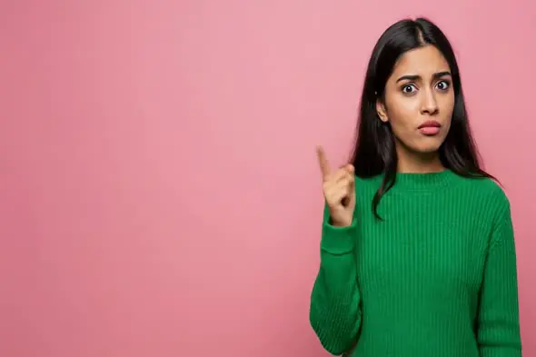 Indian Woman Pointing Up with Alert Expression on Pink Background