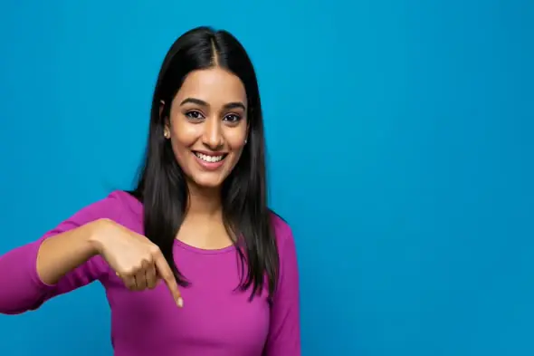 Smiling Indian Woman Pointing Down on Blue Background