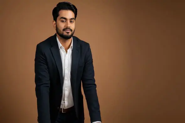 Confident Indian Businessman in Formal Attire Standing Against Brown Background