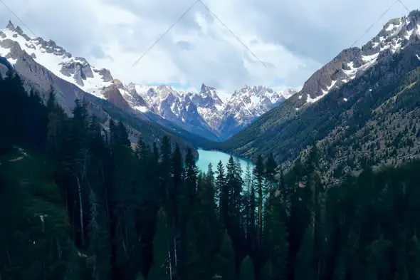 Aerial View of Mountain Lake Surrounded by Snow-Capped Peaks and Evergreen Forest