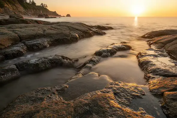 Serene Coastal Sunrise Illuminating Rocky Shore Scenery
