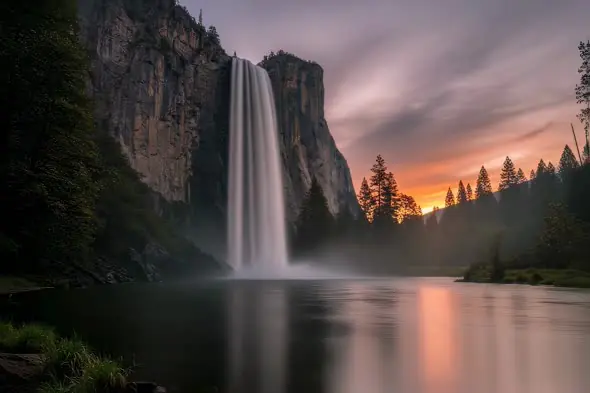 Majestic Waterfall Cascades Against Vibrant Sunset Mountain Backdrop